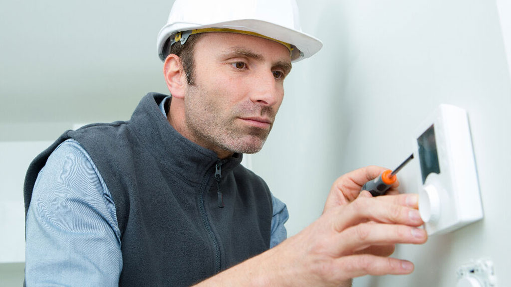 Électricien installant un thermostat connecté sur un mur dans une maison d'Étampes